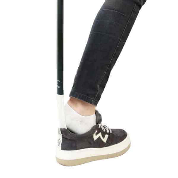 Skohorn och skotagare används för att enkelt ta på en sneaker, som visas på en fot med en svart jeans.