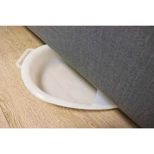 sängbäcken med handtag i plast syns delvis under en soffa med handtag synliga för enkel hantering.