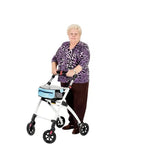 Rullator inomhus Äldre kvinna som går med smal vit rollator med blå korg på vit bakgrund.