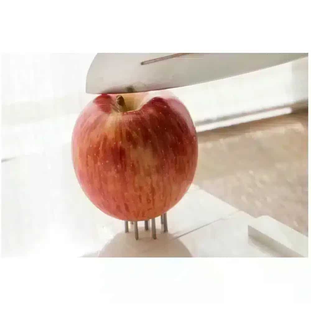 Multifunktionell skärbräda med kniv som skär en äpple, vilket visar skärbrädans klämfunktion.