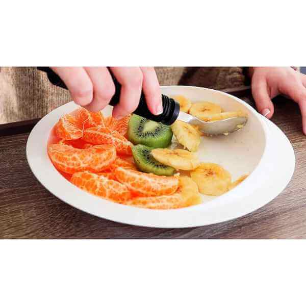 Tallrik med hög kant och sugkopp med frukt, en hand använder sked för att ta upp banan och kiwi.