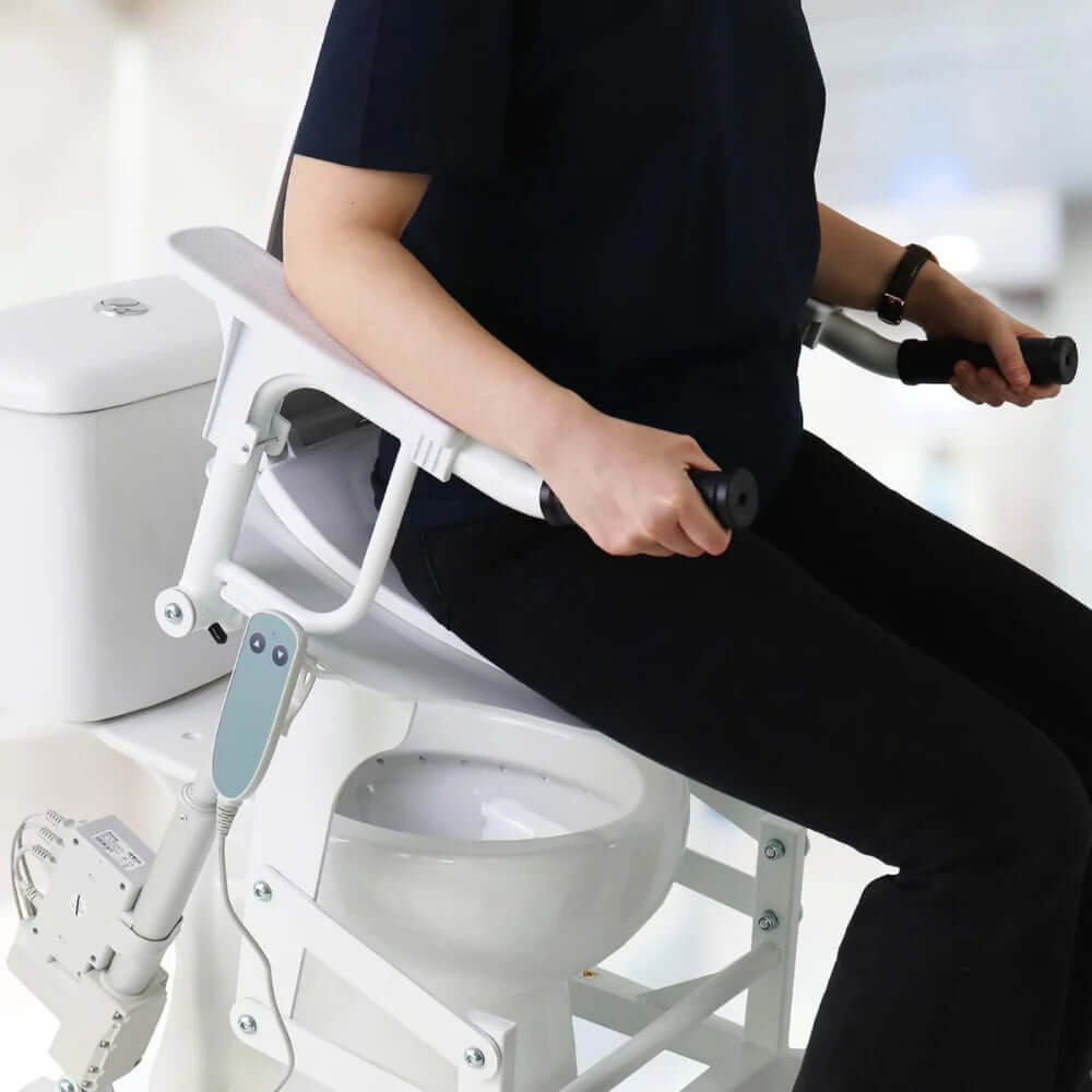 Användare sitter på den Elektrisk toalettsitsförhöjare Kmina med armstöd och handtag för stöd.