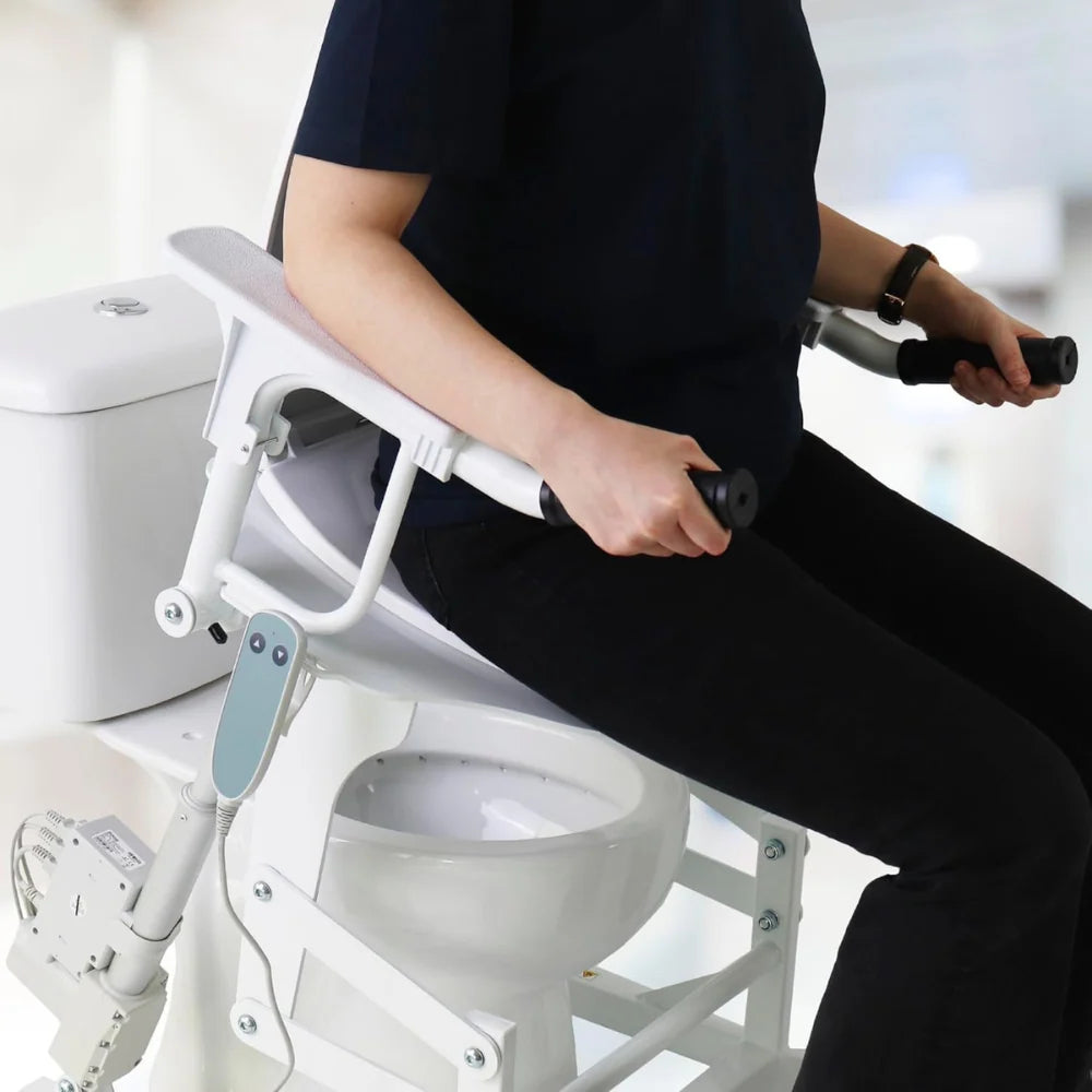 Användare sitter på den Elektrisk toalettsitsförhöjare Kmina med armstöd och handtag för stöd.