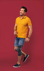 En man med knästöd Genu Dynastab går leende i en gul polo och jeansshorts.