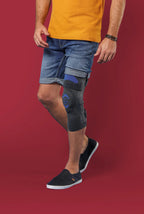Man wearing shorts and shoes with Knästöd Genu Dynastab knee support on a red background.