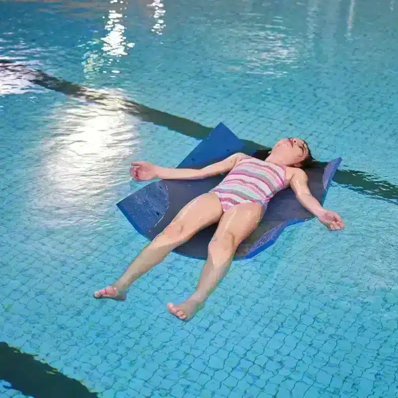 Barn använder vattenterapimatta i bassäng Barn liggande på vattenterapimatta i bassäng – demonstrerar flytkraft och avslappning.