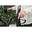 Person som håller i handtagen på en svart hopfällbar rollator med bromsfunktion.