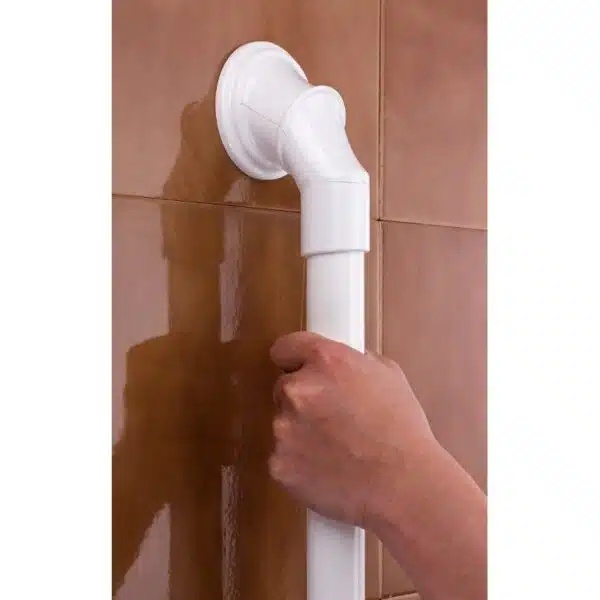 Hand som håller i ett vitt säkerhetshandtag med sugproppar på kakelvägg i badrum.
