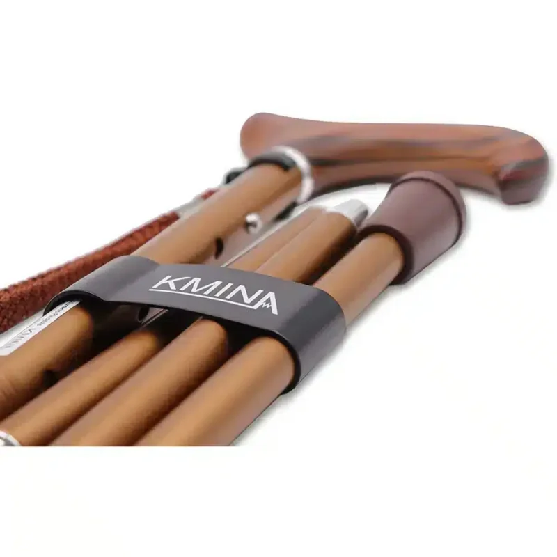 Hopfälld käpp med trähandtag – närbild Hopfälld bronsfärgad käpp med trähandtag och elastiskt band.