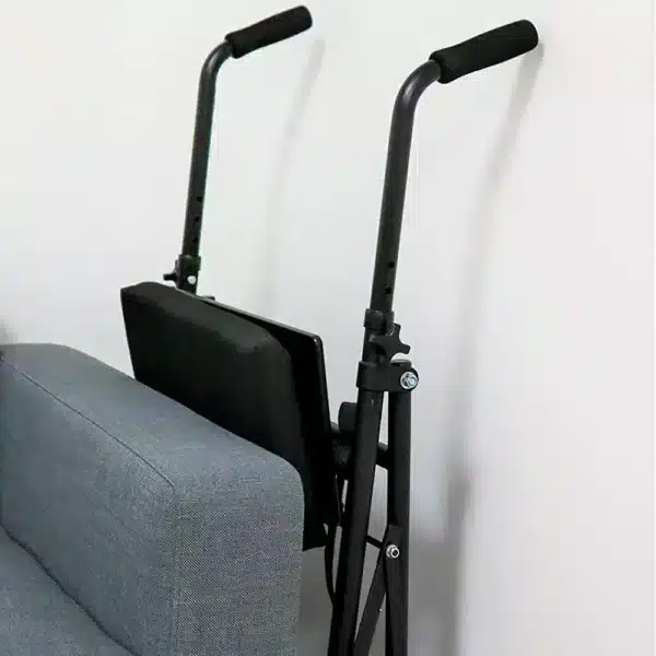 Hopfälld rullator med två hjul lutad mot en soffa för kompakt förvaring.