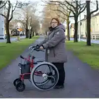 Woman walking with Wheellator in rollator position on walkway with trees.