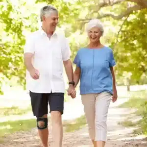 Äldre man som promenerar med knäskydd tillsammans med kvinna i park.