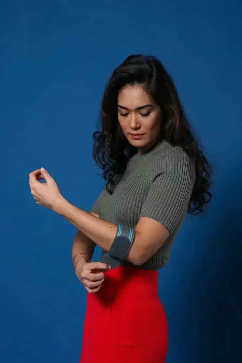 Användning av ortos för tennisarmbåge Kvinna justerar ortos för tennisarmbåge på vänster arm